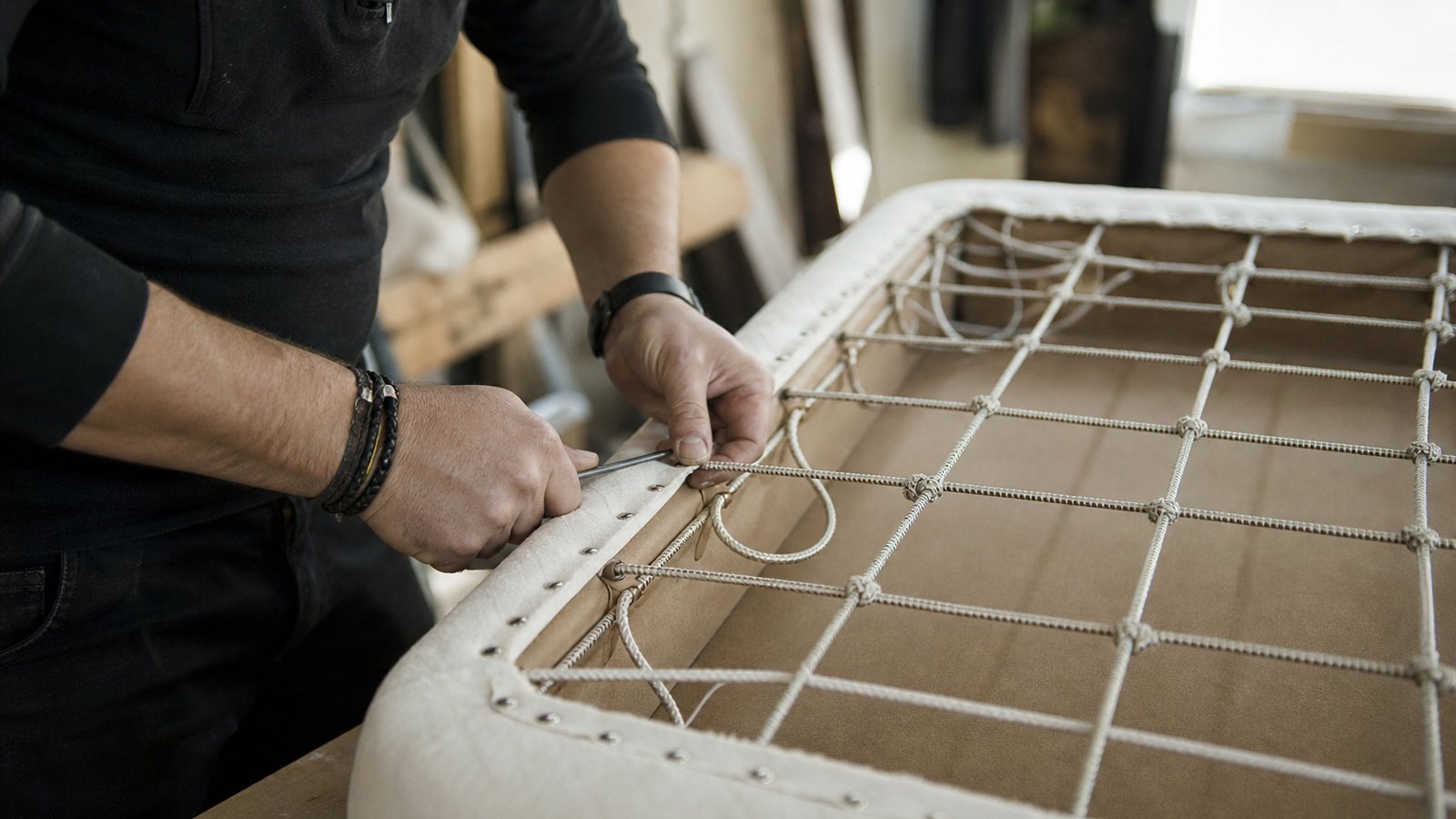 Mains d'un artisan tapissier piquant et capitonnant un matelas à la main dans son atelier
